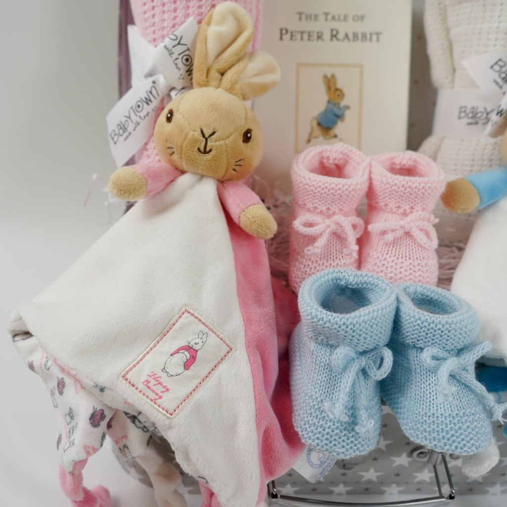 twin hamper with Beatrix potter flopsy bunny comforter in pink and white ab=nd blue and white Peter Rabbit comforter, baby booties in pink and blue, Peter rabbit book, pink cellular blanket, white cellular blanket