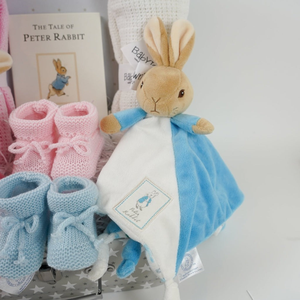 twin hamper with Beatrix potter flopsy bunny comforter in pink and white ab=nd blue and white Peter Rabbit comforter, baby booties in pink and blue, Peter rabbit book, pink cellular blanket, white cellular blanket