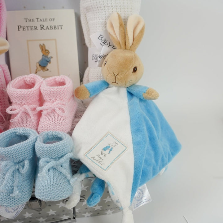 twin hamper with Beatrix potter flopsy bunny comforter in pink and white ab=nd blue and white Peter Rabbit comforter, baby booties in pink and blue, Peter rabbit book, pink cellular blanket, white cellular blanket