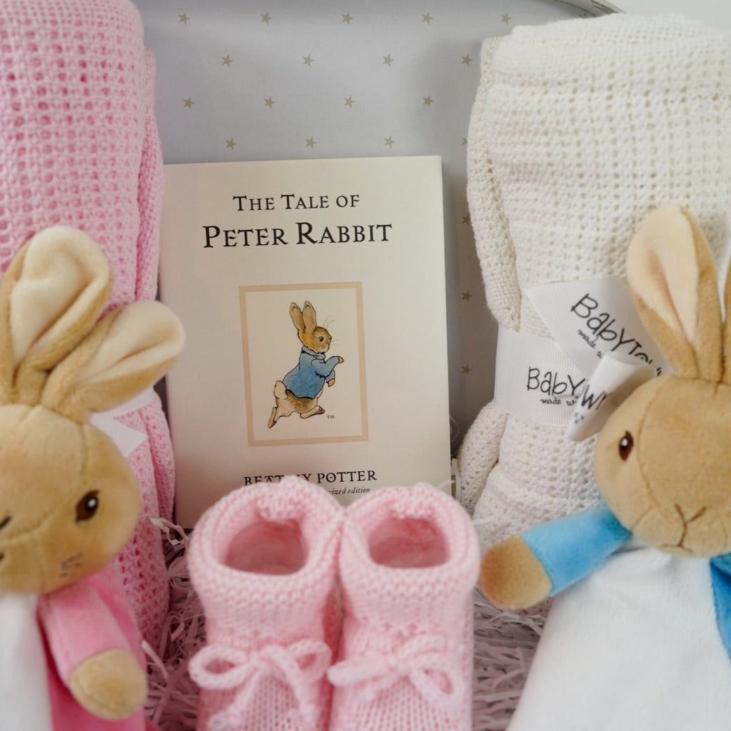 twin hamper with Beatrix potter flopsy bunny comforter in pink and white ab=nd blue and white Peter Rabbit comforter, baby booties in pink and blue, Peter rabbit book, pink cellular blanket, white cellular blanket