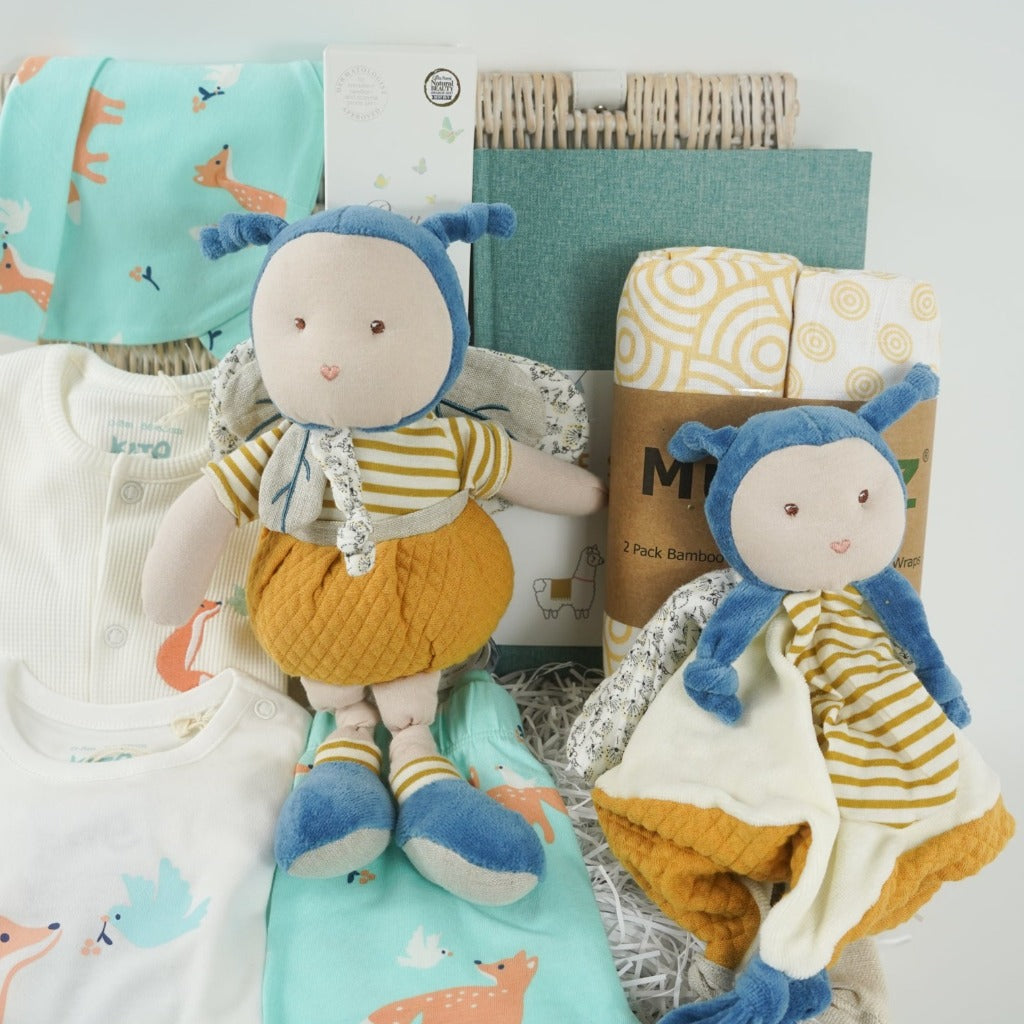 Baby hamper with organic clothing set includes baby sleepsuit in white with fox and dove design, baby bodysuit with long sleeves and fox and dove design, baby leggings with fox and matching hat, Organic cotton bee soft toy and matching comforter, organic cotton white swaddles with yellow design, green baby journal, organic baby toiletries