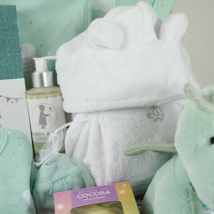 baby hamper basket, baby journal, baby layette outfit in pale mint green with elephants , white baby dressing gown with cute ears, white hot chocolate bomb, baby organic bubble bath, Dragon taggie in green and matching taggie book , white knit booties