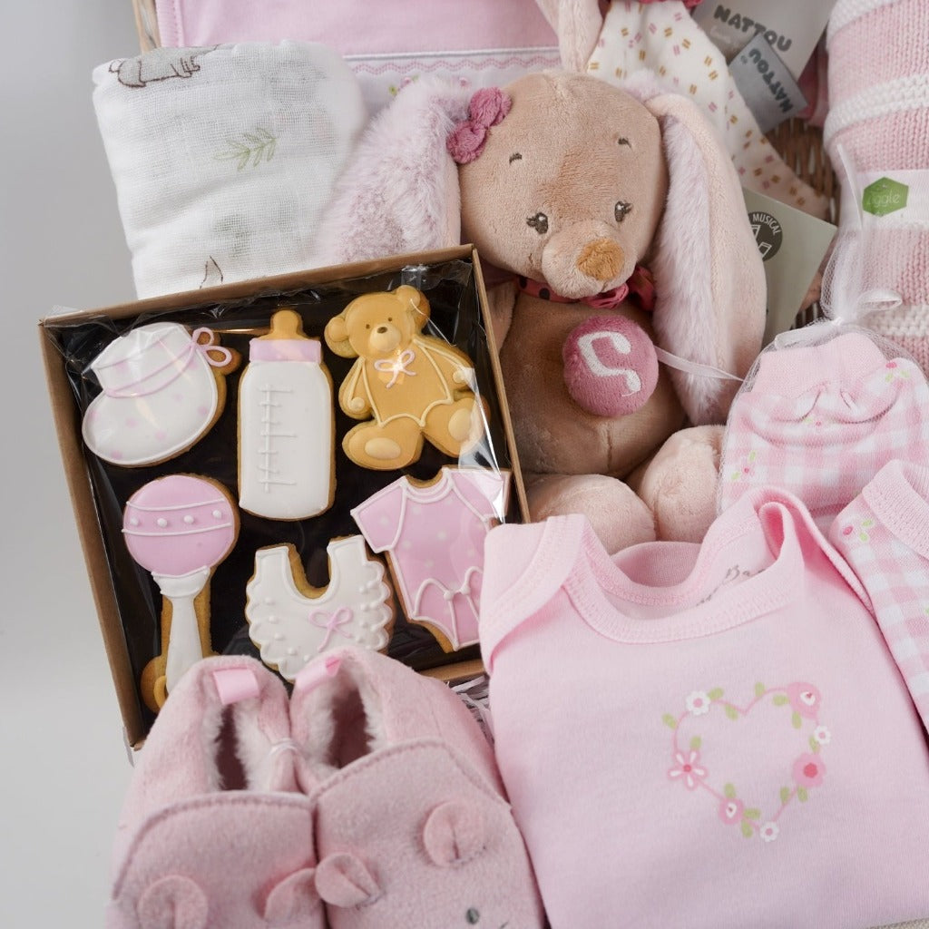 baby hamper basket with baby themed biscuits for mum, baby white muslin with bunnies, pink layette, musical  baby bunny and matching comforter, baby pink shoes with cute ears , pink and white knit blanket