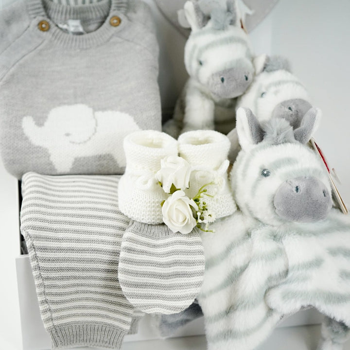 unisex baby hamper, grey knit elephant jumper, grey and white stripped leggings, grey and white hat and baby mitens, grey and white zebra comforter, baby rattle and plush zebra soft toy, white baby booties, grey baby nursery plaque