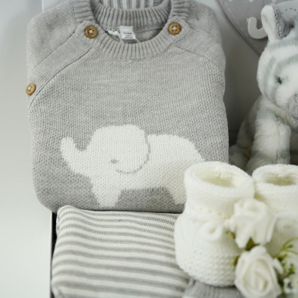 unisex baby hamper, grey knit elephant jumper, grey and white stripped leggings, grey and white hat and baby mitens, grey and white zebra comforter, baby rattle and plush zebra soft toy, white baby booties, grey baby nursery plaque