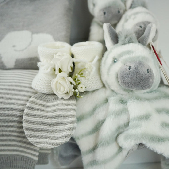 unisex baby hamper, grey knit elephant jumper, grey and white stripped leggings, grey and white hat and baby mitens, grey and white zebra comforter, baby rattle and plush zebra soft toy, white baby booties, grey baby nursery plaque