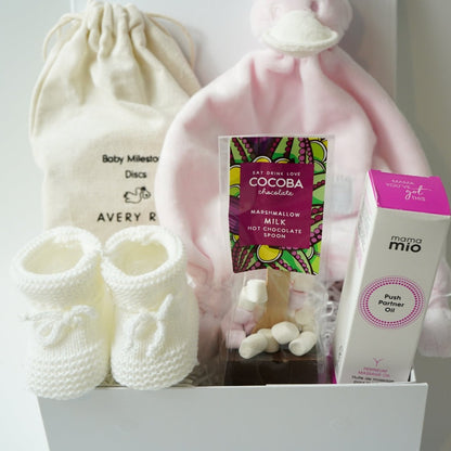 pregnancy hamper with wooden pregnancy milestone discs in a draw string bag, white knit booties, pink BamBam duck tuttle, perineum oil