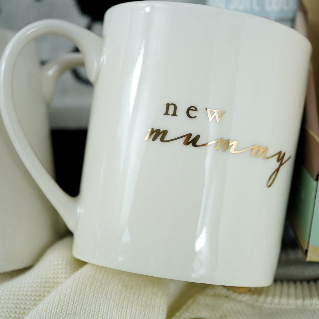 Neutral baby gift hamper, baby jumper in cream with black teddy face and matching cream joggers, New mummy and New daddy cream mugs with gold writing, wooden baby rattle, Black and cream teddy face baby blanket, organic baby lotion