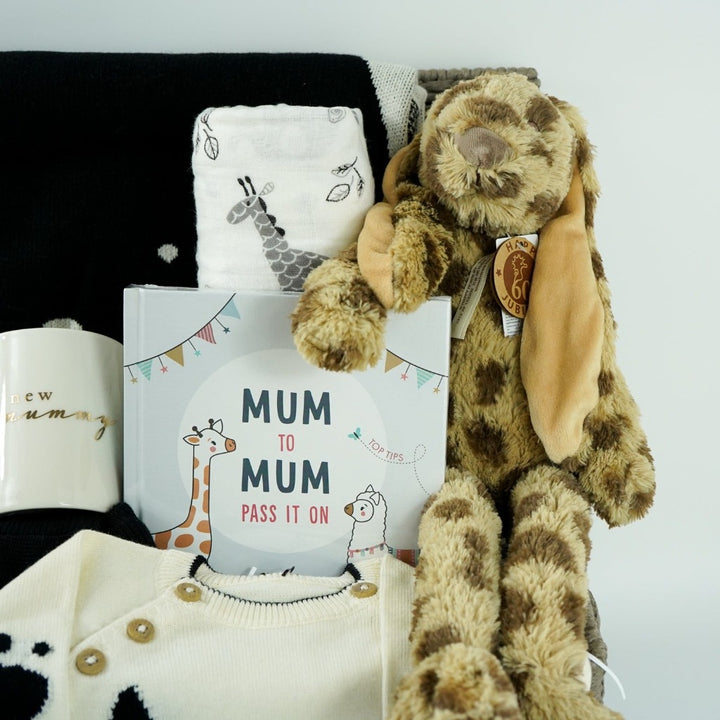 baby hamper with organic baby clothing set in black and cream with bunny face, matching black and cream organic cotton baby blanket with bunny face, white swaddle with grey giraffes, cream porcelain mug with new mummy in gold lettering, leopard print fluffy bunny soft toy, mum advice and tips hard back book