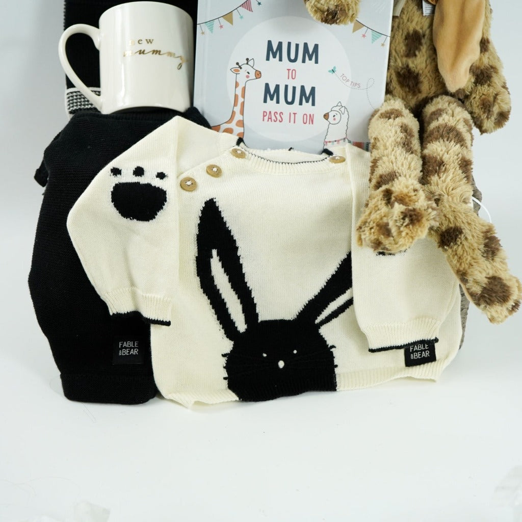 baby hamper with organic baby clothing set in black and cream with bunny face, matching black and cream organic cotton baby blanket with bunny face, white swaddle with grey giraffes, cream porcelain mug with new mummy in gold lettering, leopard print fluffy bunny soft toy, mum advice and tips hard back book