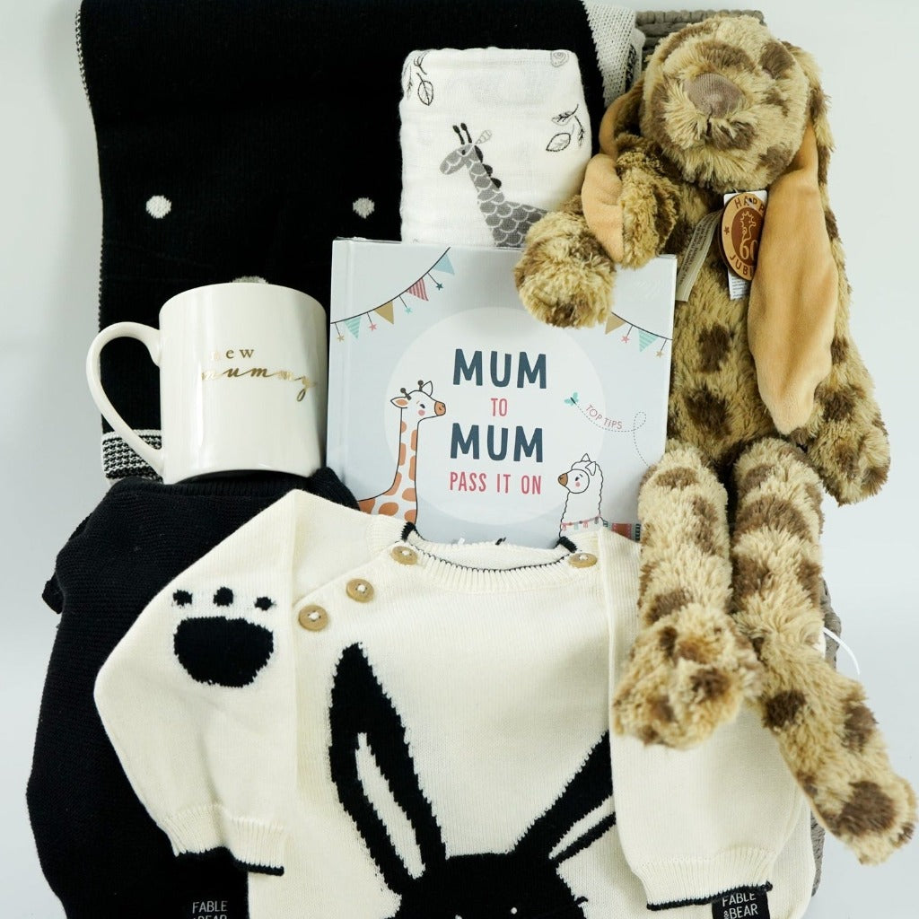 baby hamper with organic baby clothing set in black and cream with bunny face, matching black and cream organic cotton baby blanket with bunny face, white swaddle with grey giraffes, cream porcelain mug with new mummy in gold lettering, leopard print fluffy bunny soft toy, mum advice and tips hard back book