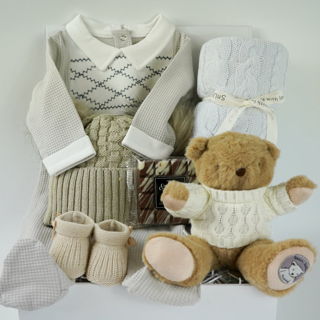 neutral baby hamper, spanish baby romper, white cotton baby wrap, baby booties, soft brown teddy with a jumper, chocolate slab, baby bobble hat