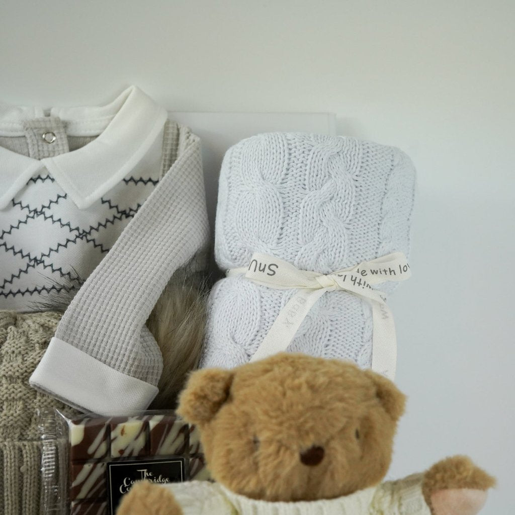 neutral baby hamper, spanish baby romper, white cotton baby wrap, baby booties, soft brown teddy with a jumper, chocolate slab