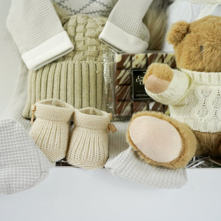 neutral baby hamper, spanish baby romper, white cotton baby wrap, baby booties, soft brown teddy with a jumper, chocolate slab