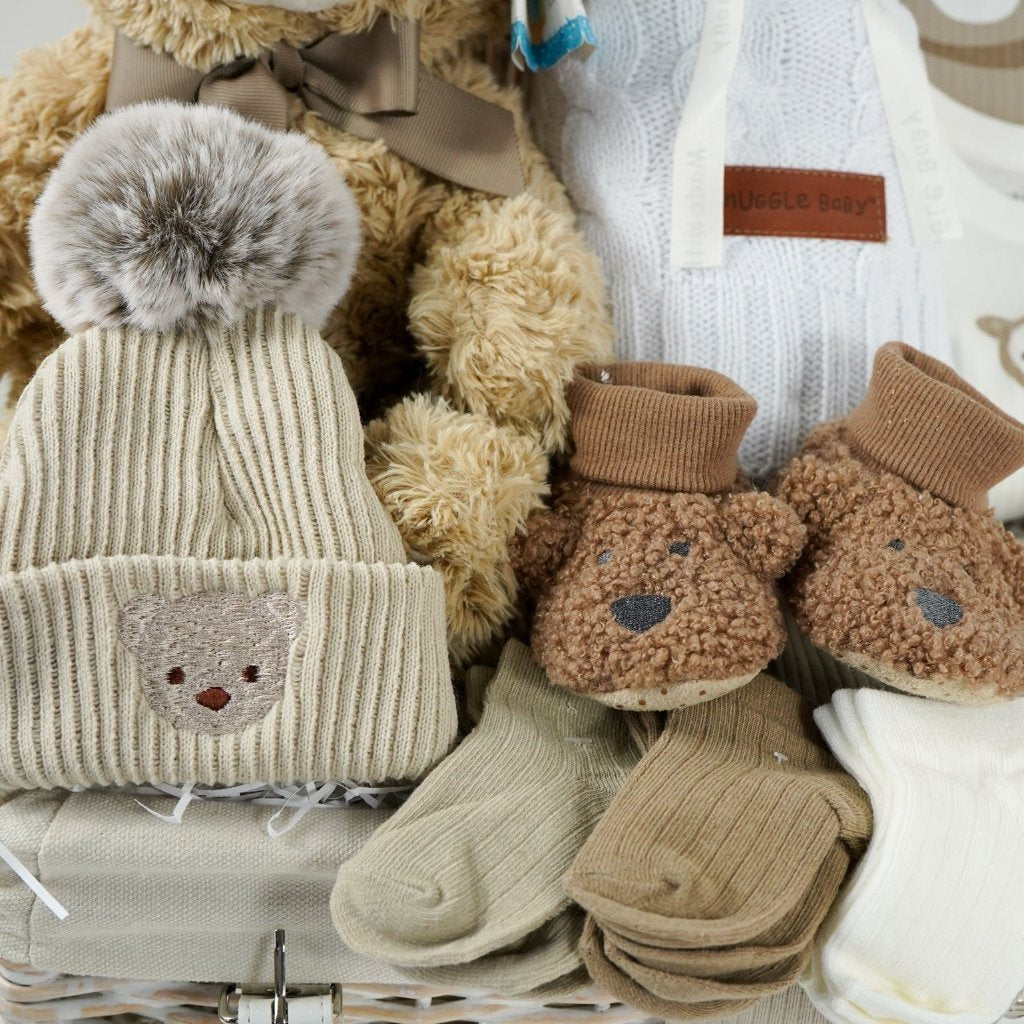 baby hamper with soft brown teddy, beige baby knit hat with embroidered teddy and pompom, white cable knit baby wrap, brown teddy bear slippers, 6 sets of baby socks in cream, brown and caramel, baby clothing set in caramel with teddy bears 