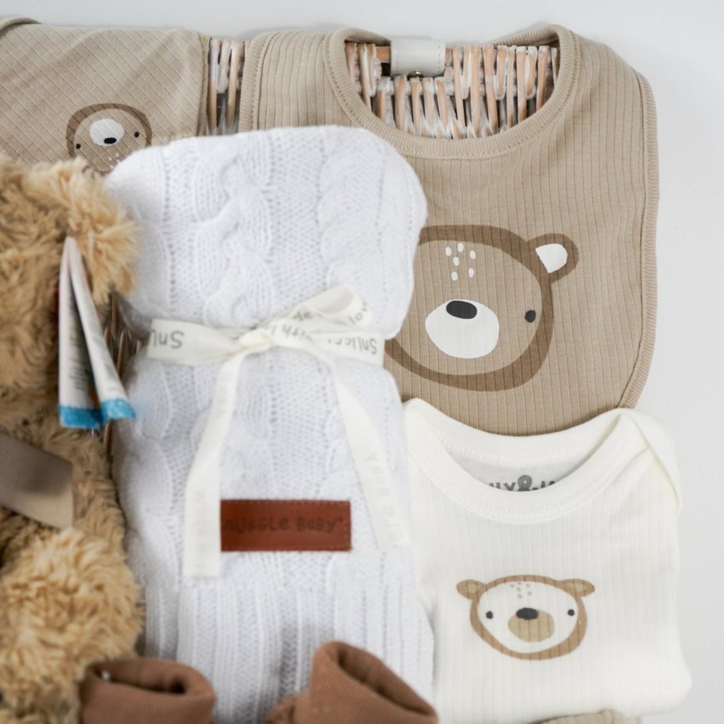 baby hamper with soft brown teddy, beige baby knit hat with embroidered teddy and pompom, white cable knit baby wrap, brown teddy bear slippers, 6 sets of baby socks in cream, brown and caramel, baby clothing set in caramel with teddy bears 