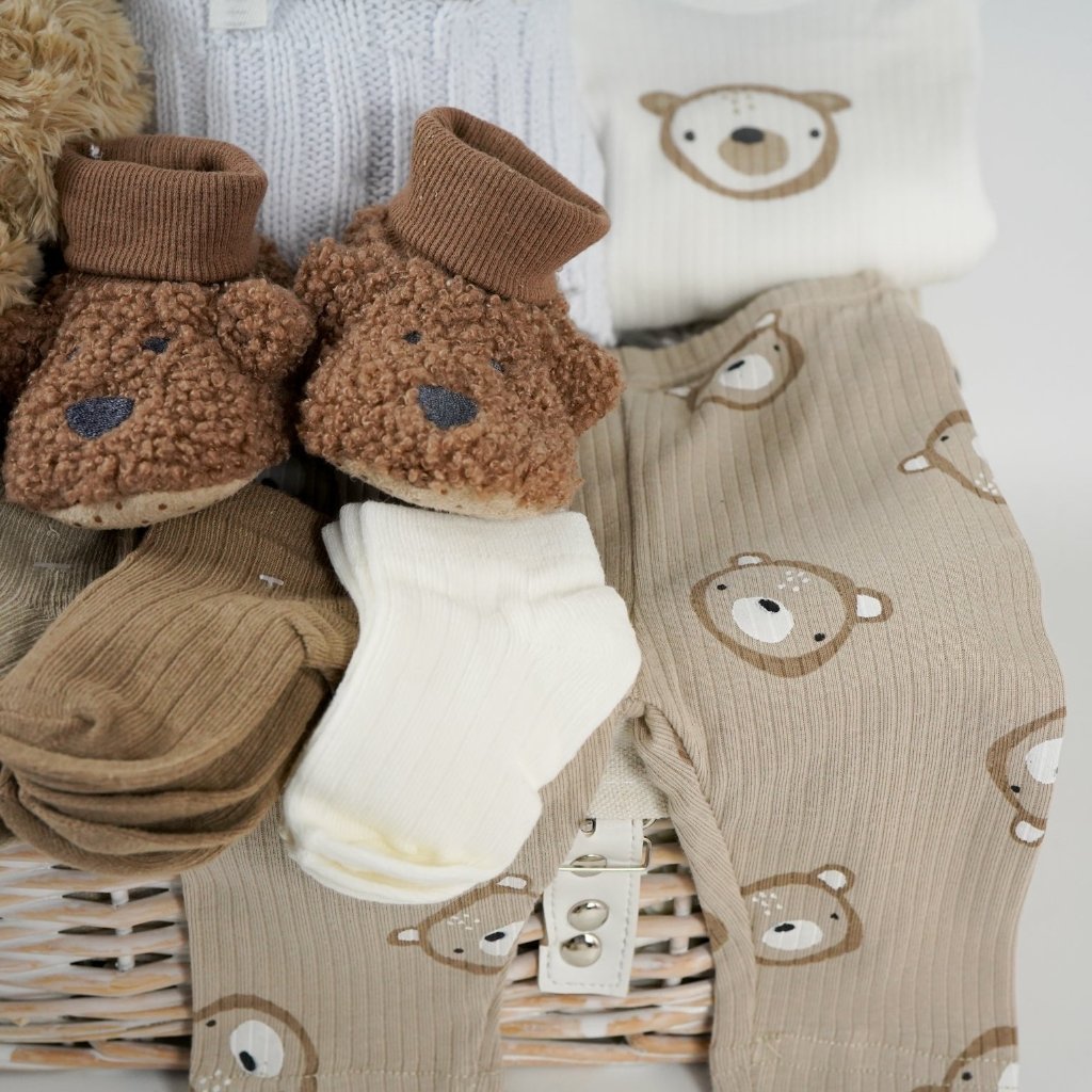 baby hamper with soft brown teddy, beige baby knit hat with embroidered teddy and pompom, white cable knit baby wrap, brown teddy bear slippers, 6 sets of baby socks in cream, brown and caramel, baby clothing set in caramel with teddy bears 