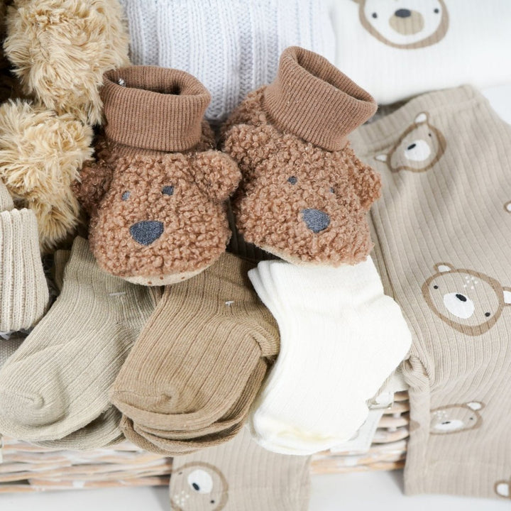 baby hamper with soft brown teddy, beige baby knit hat with embroidered teddy and pompom, white cable knit baby wrap, brown teddy bear slippers, 6 sets of baby socks in cream, brown and caramel, baby clothing set in caramel with teddy bears 