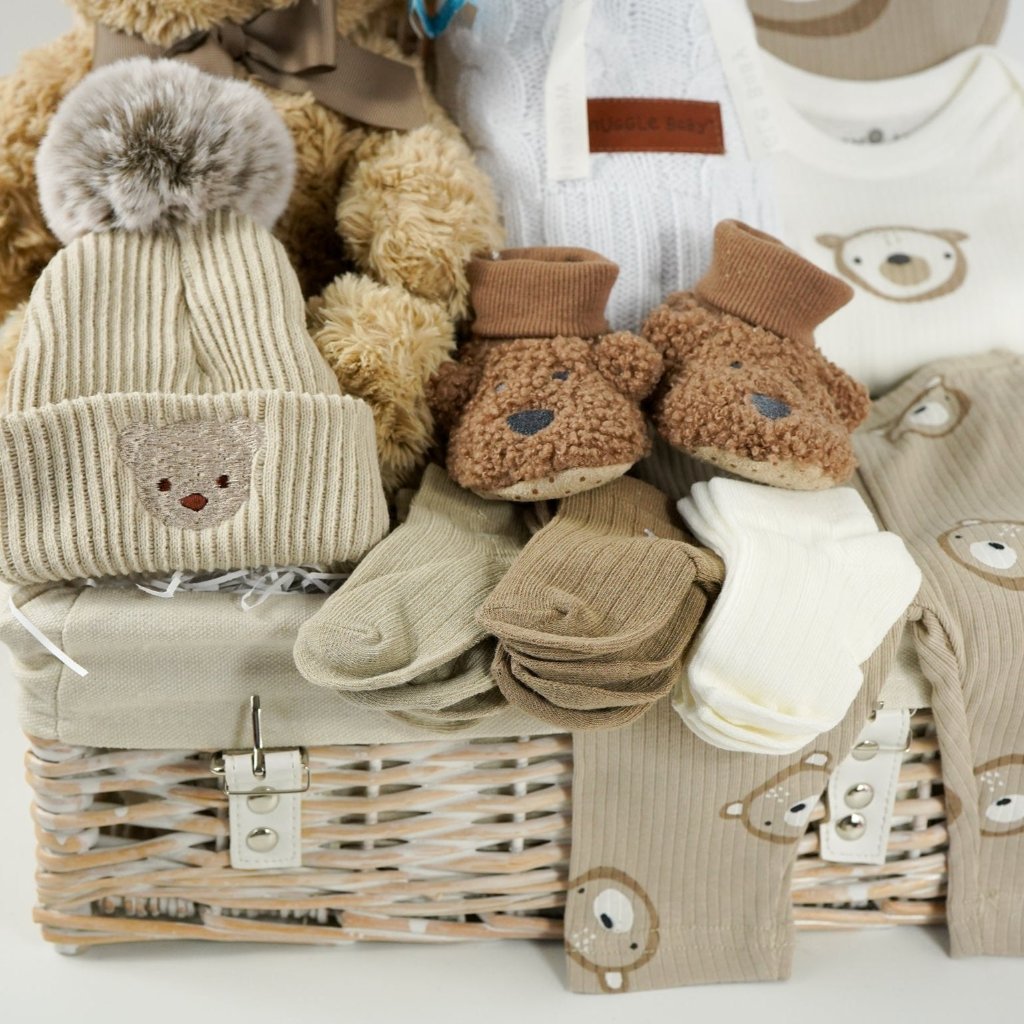 baby hamper with soft brown teddy, beige baby knit hat with embroidered teddy and pompom, white cable knit baby wrap, brown teddy bear slippers, 6 sets of baby socks in cream, brown and caramel, baby clothing set in caramel with teddy bears 