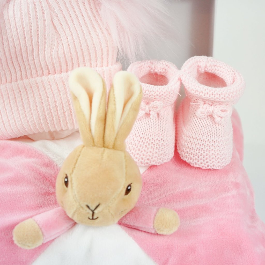 small white hamper box with beatrix potter pink bunny comforter with knot ends , pink booties and pink double pompom fluffy 