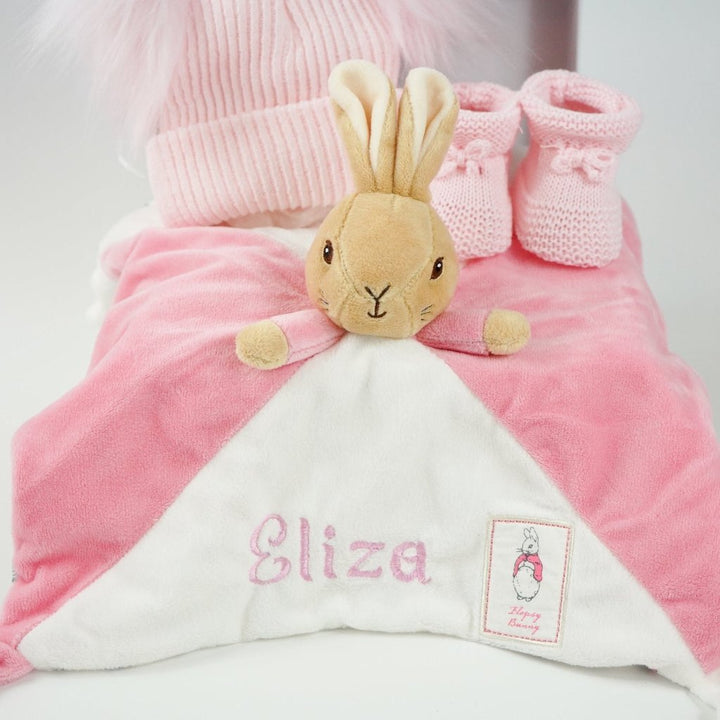 small white hamper box with beatrix potter pink bunny comforter with knot ends , pink booties and pink double pompom fluffy 