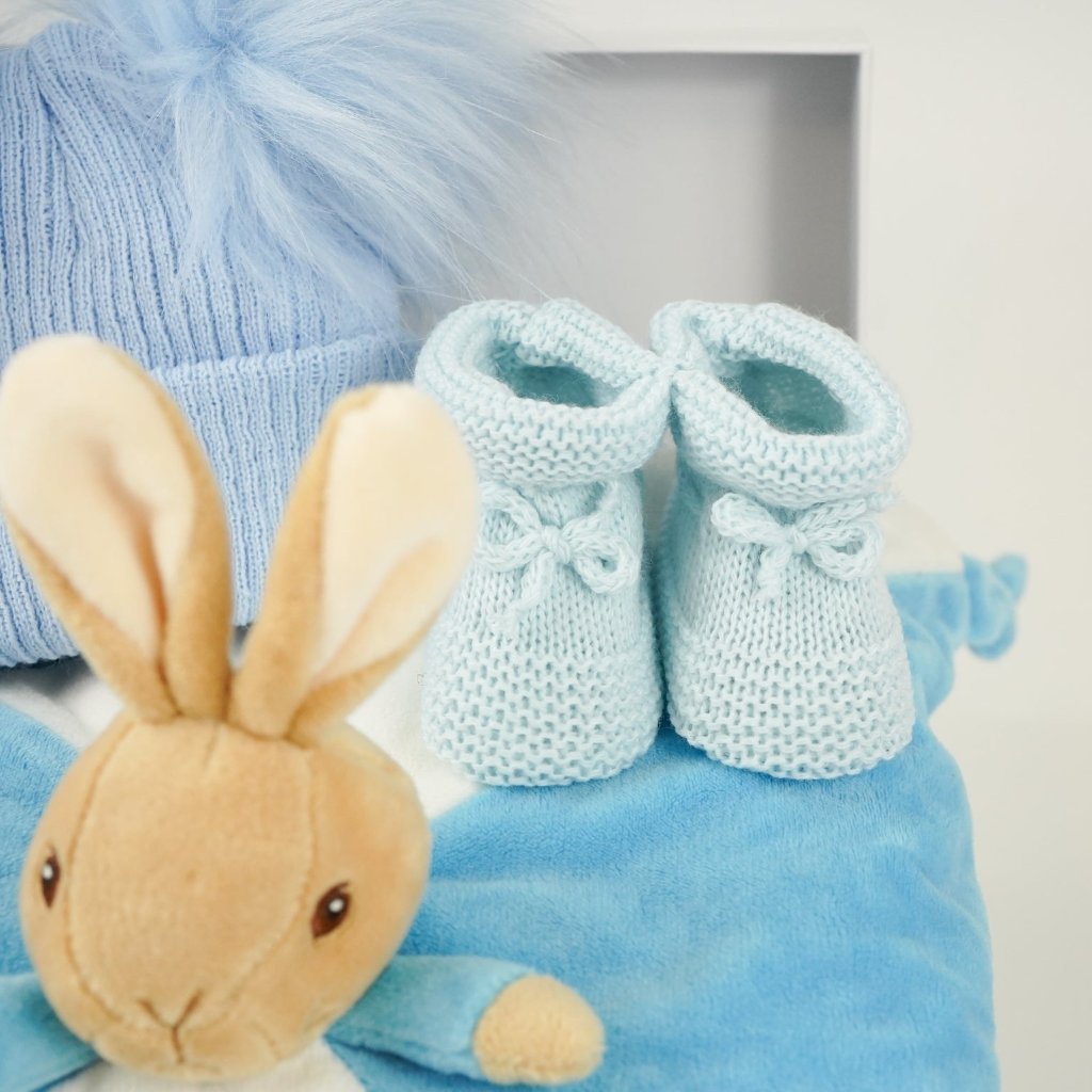 blue baby hamper with Peter Rabbit baby comforter , blue double pompom hat and blue knit booties 