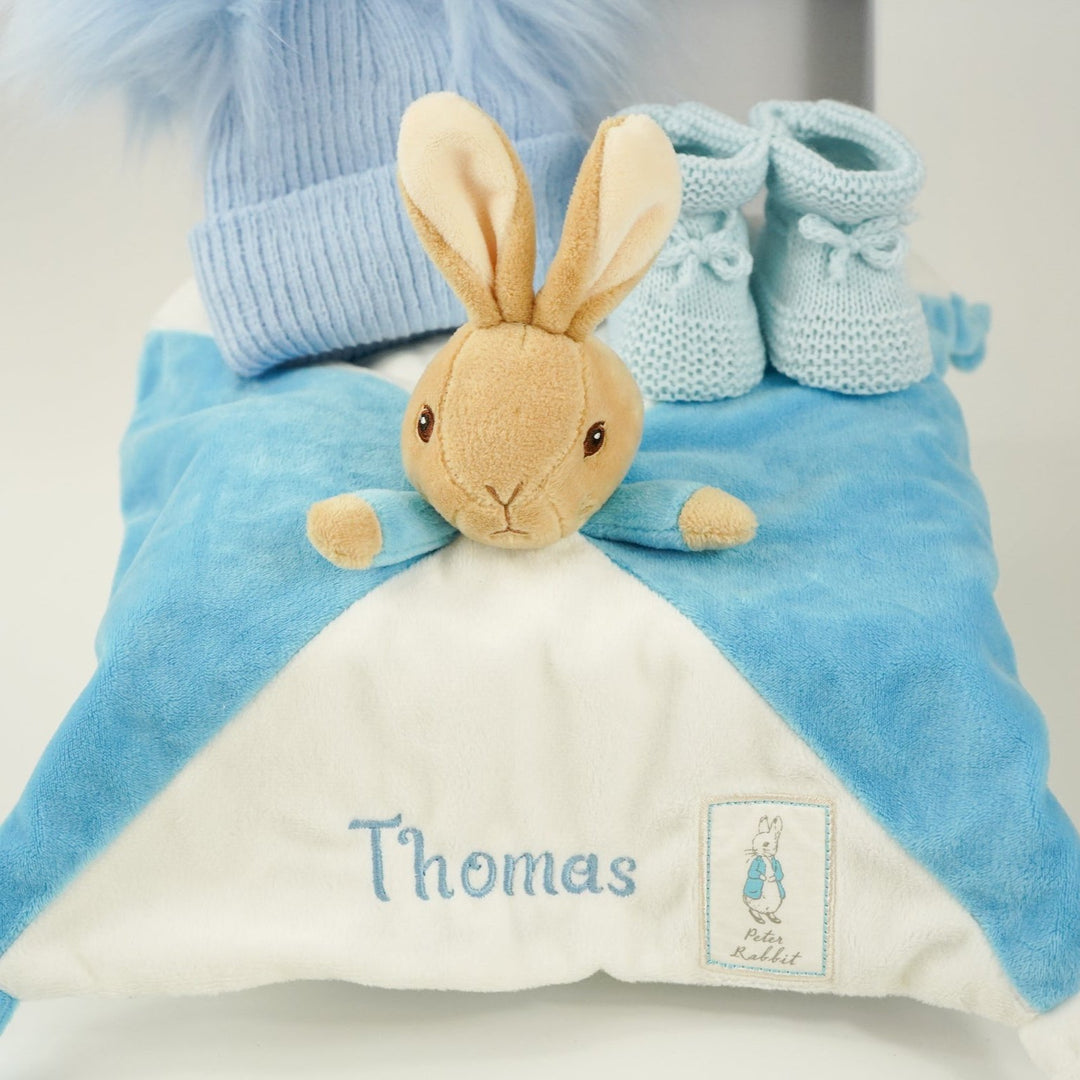 blue baby hamper with Peter Rabbit baby comforter , blue double pompom hat and blue knit booties 