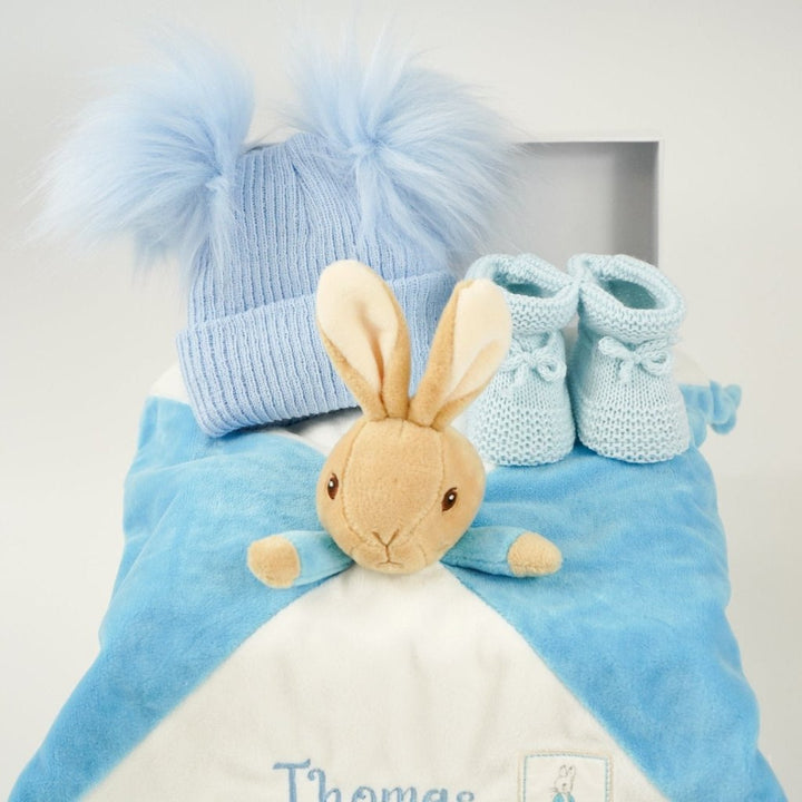 blue baby hamper with Peter Rabbit baby comforter , blue double pompom hat and blue knit booties 