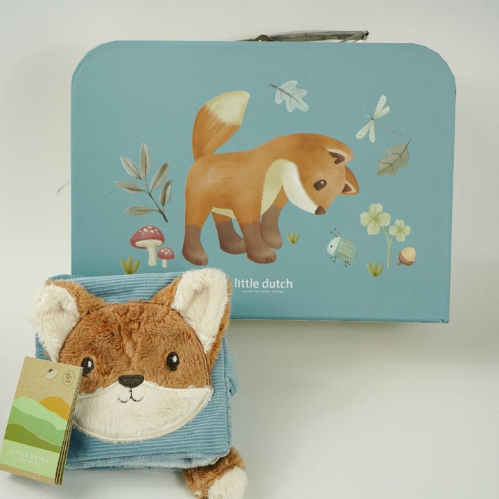 cardboard suitcase with soft activity book in blue with fox head design, fox soft rattle, chocolate spoon with mallows, blue fluffy pompom hat, two pairs of booties 