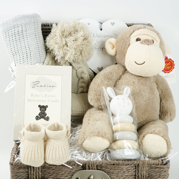 Baby grey hamper basket with grey cellular baby blanket, baby biscuit coloured pom pom hat, heart hanging nursery plaque, Baby milestone Cards, baby booties in biscuit colour, wooden stacking toy and soft eco friendly baby soft toy