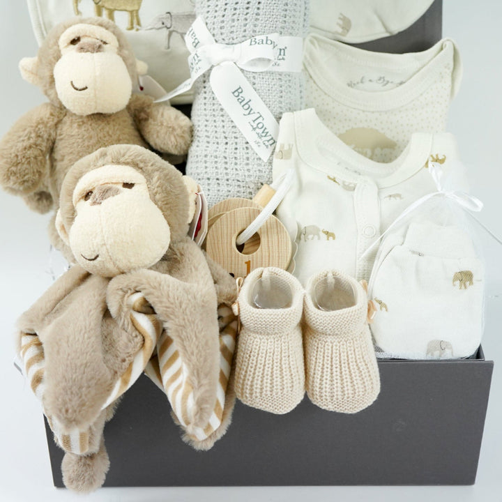 neutral baby hamper box, brown ecofriendly baby monkey comforter and matching soft toy, caramel coloured baby booties and wooden teething keys, grey soft cellular blanket, cream 100% cotton baby layette with embroidered elephants in brown and grey on the bib and printed elephants on the body