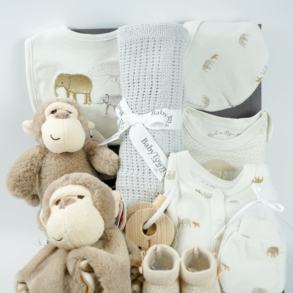 neutral baby hamper box, brown ecofriendly baby monkey comforter and matching soft toy, caramel coloured baby booties and wooden teething keys, grey soft cellular blanket, cream 100% cotton baby layette with embroidered elephants in brown and grey on the bib and printed elephants on the body