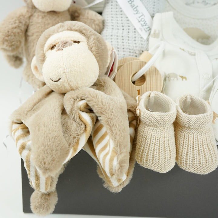 neutral baby hamper box, brown ecofriendly baby monkey comforter and matching soft toy, caramel coloured baby booties and wooden teething keys, grey soft cellular blanket, cream 100% cotton baby layette with embroidered elephants in brown and grey on the bib and printed elephants on the body