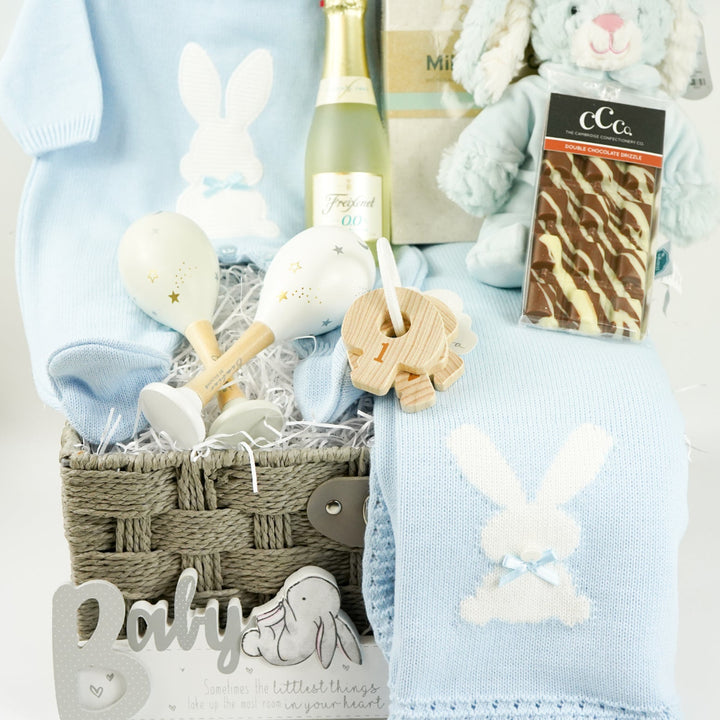 luxury baby and new parents hamper gift, blue baby blanket with white rabbit, knit blue romper with feet and white bunny, maracas, wooden teething key ring, small bottle of freixenet, chocolate, Little Dutch baby bunny milestone cards in a box, soft blue bunny in a velour pj's