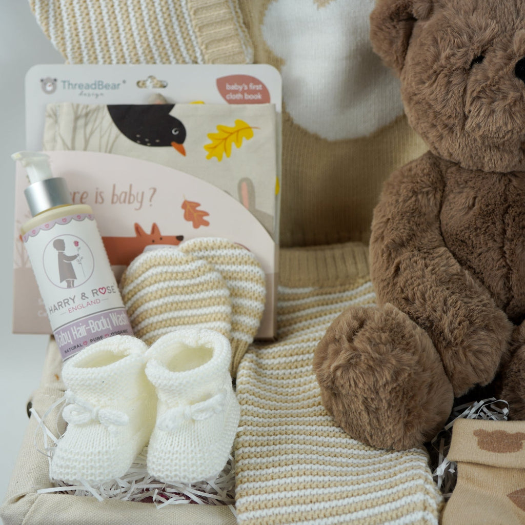 teddy bear themed baby hamper, beige and white baby knit clothing set with jumper, stripe knit leggings, hat and mittens, fabric baby book, 2 pairs of cream baby socks with teddy bear design , fabric baby book, baby shampoo and body wash, fabric book