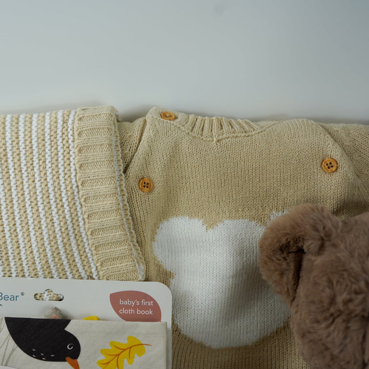 teddy bear themed baby hamper, beige and white baby knit clothing set with jumper, stripe knit leggings, hat and mittens, fabric baby book, 2 pairs of cream baby socks with teddy bear design , fabric baby book, baby shampoo and body wash, fabric book