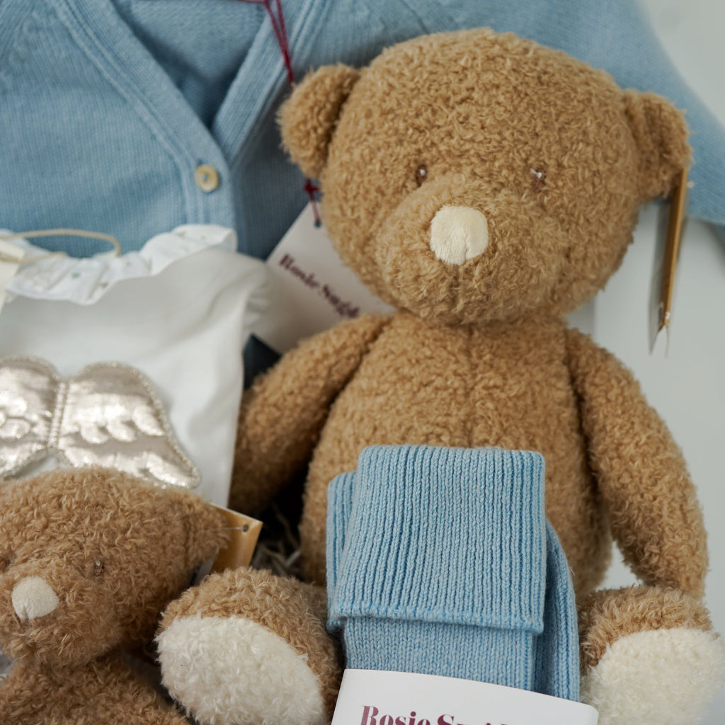 Luxury baby gift hamper box with pale blue cashmere baby cardigan, white luxury baby sleepsuit with frilled collar and silver angel wings on the back, wooden baby rattle with blue silicone teething beads, matching cashmere socks for mum in pal blue, soft teddy and matching baby comforter 