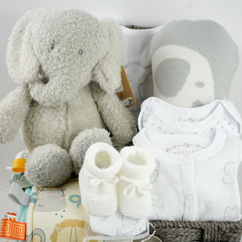 eutral baby hamper in grey rope basket, grey nattou soft elephant, grey and white soft baby blanket, taggie blanket with lion, elephants and zebras faces  with fleece backing, white baby layette set with grey elephant  design includes baby sleepsuit, baby bodysuit, hat, mittens and bib