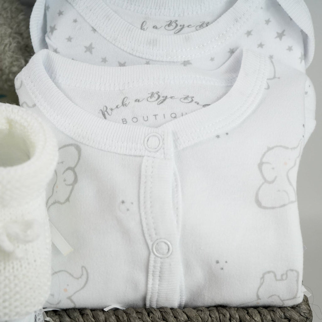 eutral baby hamper in grey rope basket, grey nattou soft elephant, grey and white soft baby blanket, taggie blanket with lion, elephants and zebras faces  with fleece backing, white baby layette set with grey elephant  design includes baby sleepsuit, baby bodysuit, hat, mittens and bib