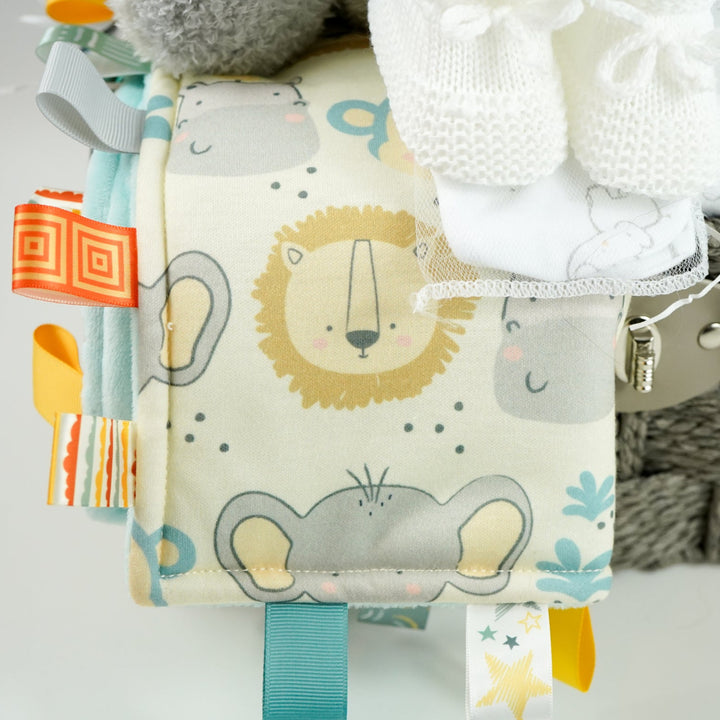 eutral baby hamper in grey rope basket, grey nattou soft elephant, grey and white soft baby blanket, taggie blanket with lion, elephants and zebras faces  with fleece backing, white baby layette set with grey elephant  design includes baby sleepsuit, baby bodysuit, hat, mittens and bib