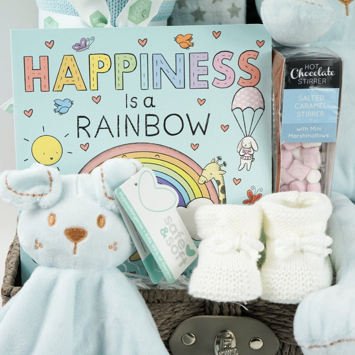hamper basket with baby blanket in blue and white stipe, soft teddy dog in blue and matching comforter,  board boo, white knit booties and white muslin square