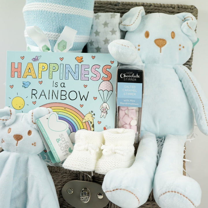 hamper basket with baby blanket in blue and white stipe, soft teddy dog in blue and matching comforter,  board boo, white knit booties and white muslin square