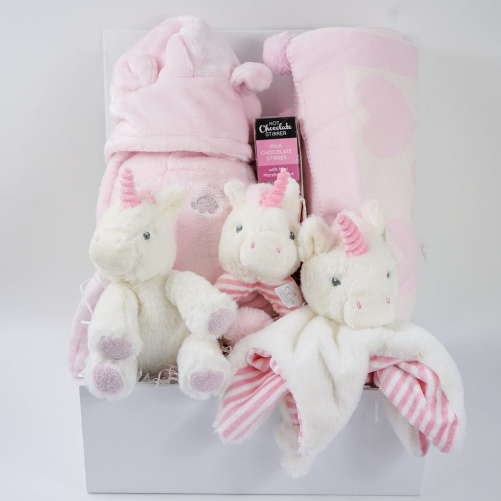 white hamper box with pink baby gown, soft eco friendly unicorn oft toy, unicorn rattle and baby comforter , pink and cream baby blanket with hearts and pom poms, chocolate stirrer spoon