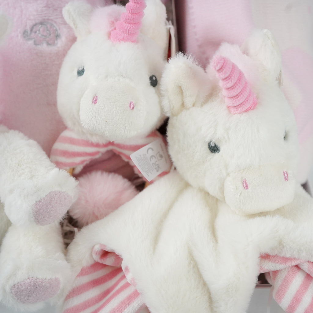 white hamper box with pink baby gown, soft eco friendly unicorn oft toy, unicorn rattle and baby comforter , pink and cream baby blanket with hearts and pom poms, chocolate stirrer spoon
