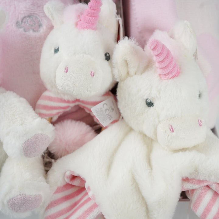 white hamper box with pink baby gown, soft eco friendly unicorn oft toy, unicorn rattle and baby comforter , pink and cream baby blanket with hearts and pom poms, chocolate stirrer spoon
