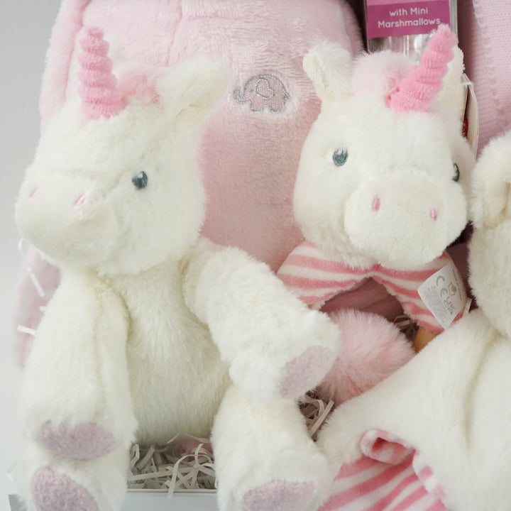 white hamper box with pink baby gown, soft eco friendly unicorn oft toy, unicorn rattle and baby comforter , pink and cream baby blanket with hearts and pom poms, chocolate stirrer spoon