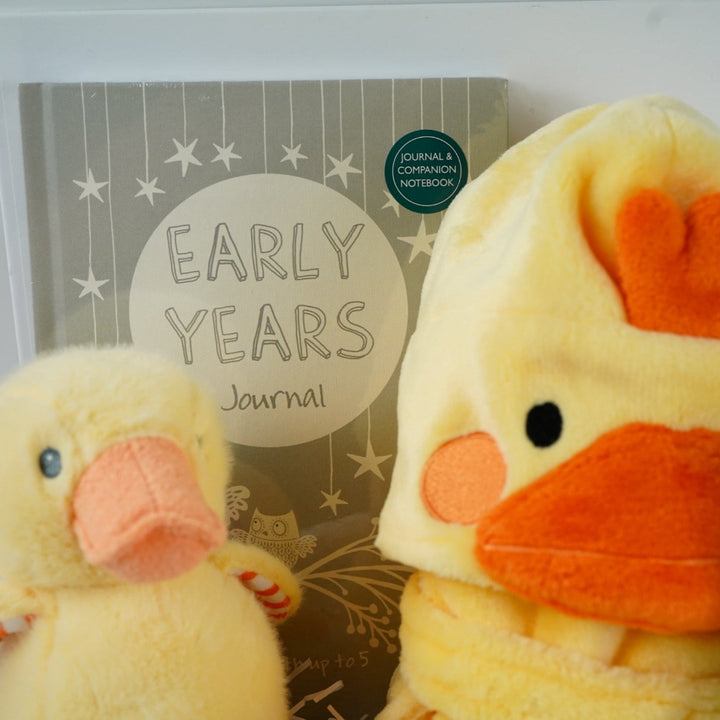 white hamper box with yellow baby dressing gown with duck face hood, soft cuddly yellow duck toy, white muslin square with yellow duck pattern., white knit baby booties, white baby sleep suit with zebra, giraffe and elephant and applique NEWBIE all in grey, yellow and orange, Early years baby journal 