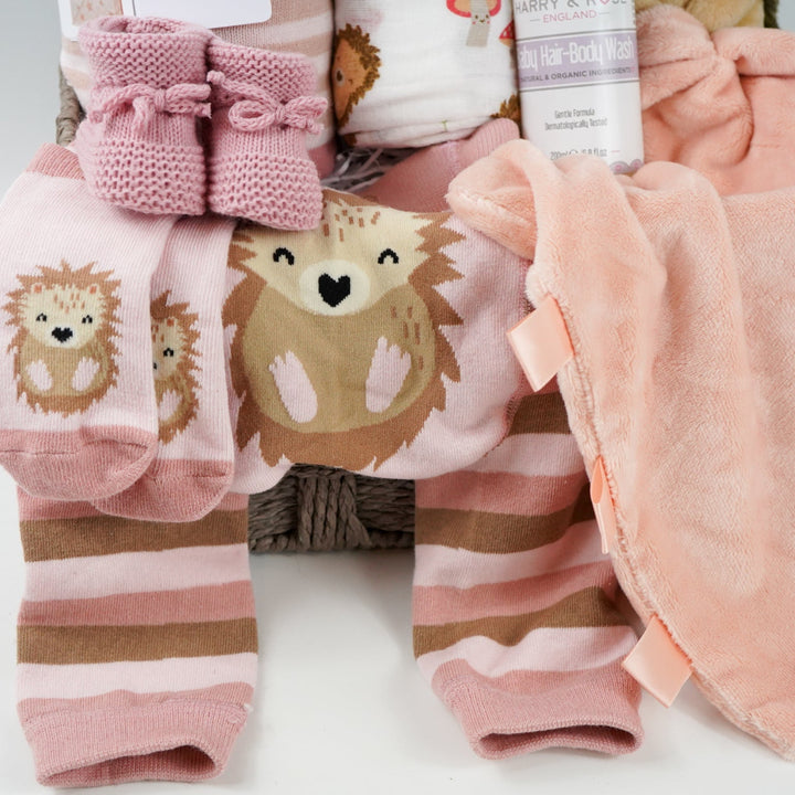 hedgehog themed baby hamper with pink striped hedgehog knit baby leggings and matching socks, baby pink star blanket, baby swaddle with hedgehogs , hedgehoge taggie comforter, baby knit booties, organic baby bath
