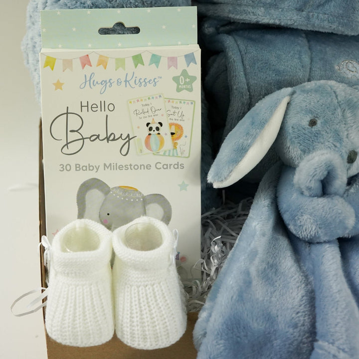Baby gift set with blue blanket, booties, and comfort toy in a box on a light blue background