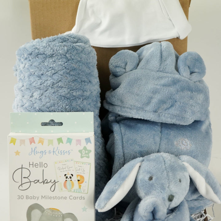 Baby gift set with blue blanket, booties, and comfort toy in a box on a light blue background